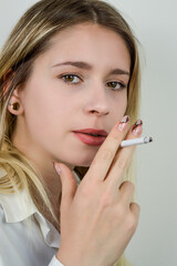 Portrait of a beautiful young blonde woman who is smoking a cigarette and is looking at camera