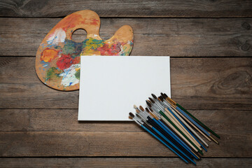 Blank canvas, brushes and palette on wooden table, flat lay. Space for text