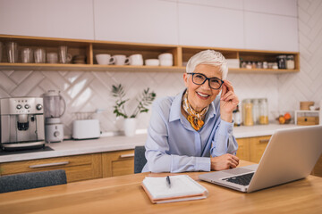 Portrait of a beautiful older woman sitting at the table with laptop and note pad.
