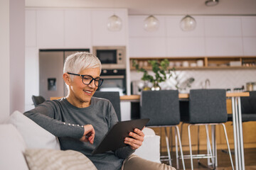 Portrait of a smiling senior woman relaxing at home, using digital tablet.