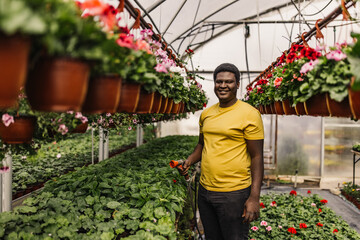 Black man in a garden smiling and holding a hose.