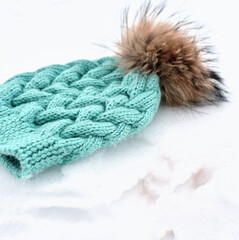 knitted turquoise hat or beanie with pom pom on a snow. winter apparel concept. kids warm clothes and accessories. knitting as a hobby