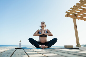 Young pregnant woman doing yoga outdoor - Meditation and maternity concept for an healthy lifestyle - Focus on face