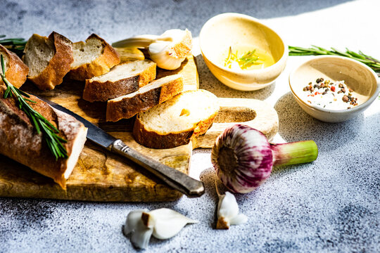 Sliced baguette loaf with a bowl of olive oil, garlic, salt, pepper and rosemary