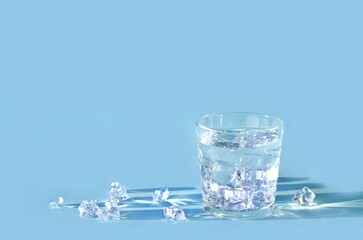 Water in glass with ice cubes on blue background, copy space