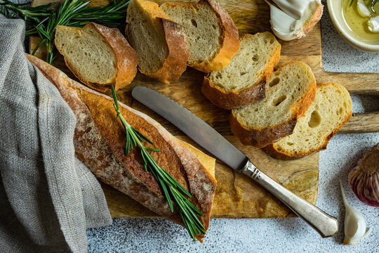 Overhead view of sliced baguette loaf with a bowl of olive oil, garlic, and rosemary