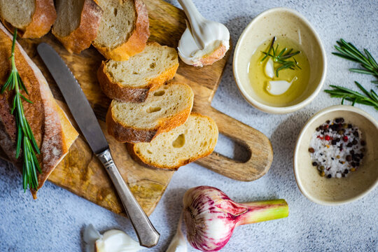 Overhead view of sliced baguette loaf with a bowl of olive oil, garlic, salt, pepper and rosemary