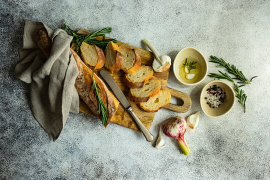 Overhead view of sliced baguette loaf with a bowl of olive oil, garlic, salt, pepper and rosemary