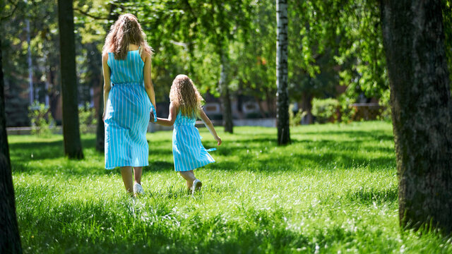Happy mother and daughter walking in the park holding hands