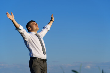 businessman poses in a field, he looks into the distance and rests, green grass and blue sky as background