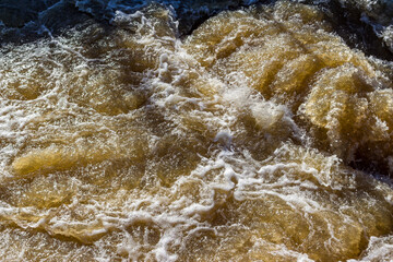 A stormy stream of water on a river dam, water with splashes and foam on the rift
