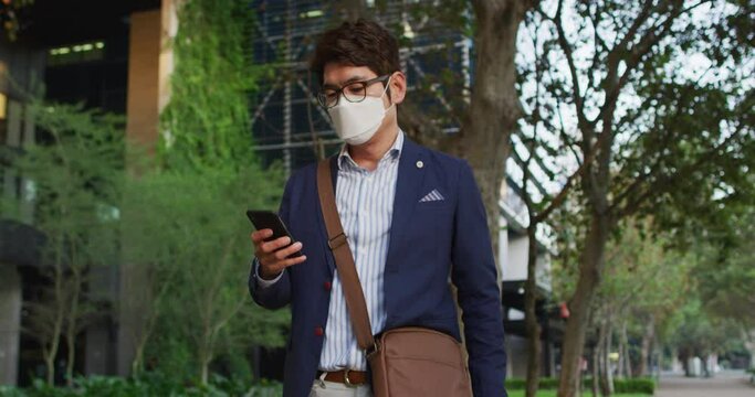 Asian man wearing face mask using smartphone while walking on the street