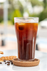 A cup of Iced Americano Coffee with ice cubes placed on a marble table in a coffee shop.
