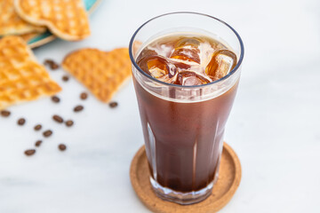 A cup of Iced Americano Coffee with ice cubes placed on a marble table in a coffee shop.