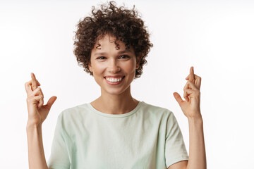 Young curly woman smiling and holding fingers crossed for good luck