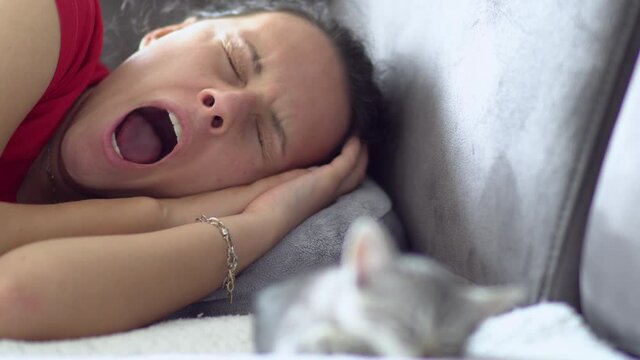 Young woman yawning while taking a nap with her adorable kitten on the sofa at home