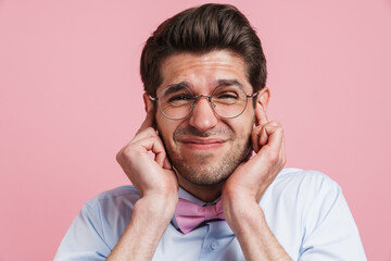 Fototapeta premium Young white man in eyeglasses frowning and plugging her ears