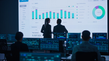Project Leader, Chief Executive Discuss Data Shown on Big Display. Screens Show Infographics,...