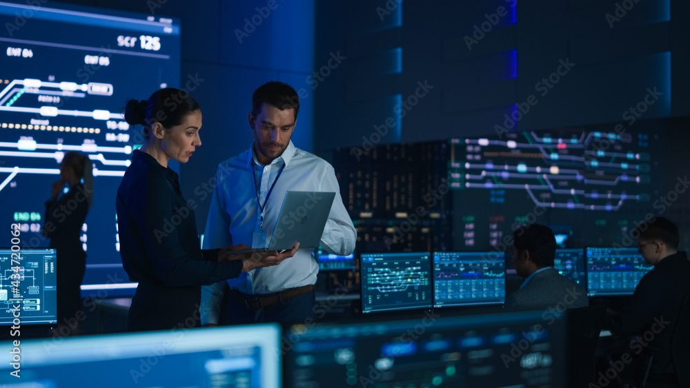 Poster Project Leader and Chief Executive Discuss Data Shown on a Laptop. In Background Big Screen Showing Infographics of Infrastructure, Charts, System Analysis. Telecommunications Control Room
