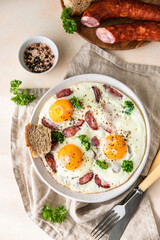 Fried eggs with sausage and parsley on a ceramic plate served with bread, light concrete background. Classic breakfast. Top view.