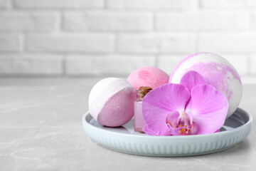 Bath bombs, bottle of oil and orchid flower on grey table, space for text