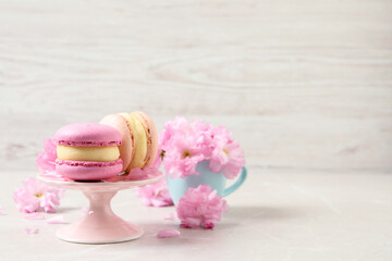 Delicious colorful macarons and pink flowers on light grey table, space for text