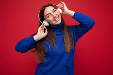 Attractive positive young brunette woman wearing blue sweater isolated over red background wall...