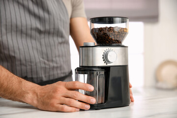 Fototapeta na wymiar Man using electric coffee grinder in kitchen, closeup