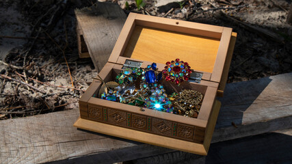 Yellow   carved wooden jewelry box with colorful  old brooches on an aged timber board.  Sparkling...