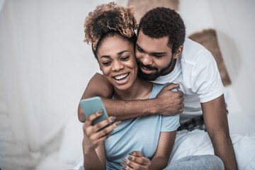 Man hugging woman sitting with smartphone