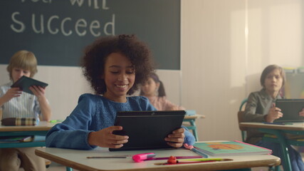 Smiling african american girl using digital tablet in class with classmates 
