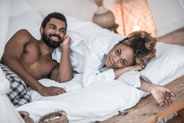 Darkskinned woman and man in home clothes in bed