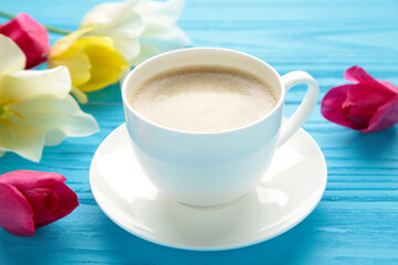 Cup of coffee with tulips on blue background