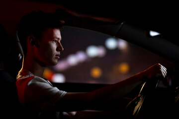 Hombre joven conduciendo de noche por la ciudad - obrazy, fototapety, plakaty