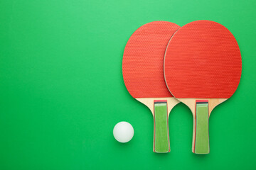 Ping pong rackets and ball on green background with copy space.