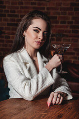 Stylish sexy woman with martini glass at table in night interior