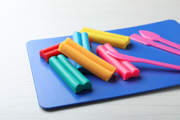 Many different colorful plasticine pieces with tools on white wooden table