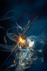 Glittering burning sparkler with smoke on blue background