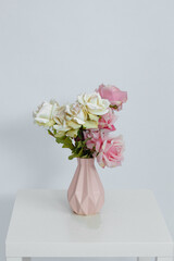 Pink vase with flowers on the table on a white background. Space for text. Close-up.