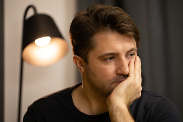 Portrait of Young unshaven handsome guy sits under spot lamp suffering from depression. Depressed...