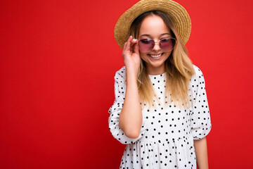 Attractive smiling young blonde woman wearing everyday stylish clothes and modern sunglasses isolated on colorful background wall looking at camera