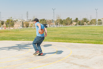 Back view of young man playing basketball in sports park.