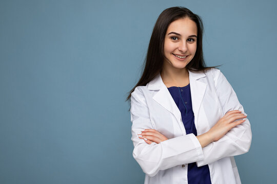 Photo portrait of young pretty beautiful positive smiling brunette woman with sincere emotions wearing white medical coat isolated over blue background with copy space and holding crossed arms