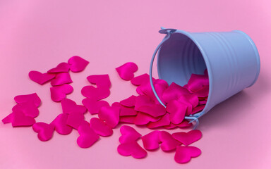 decorative hearts are scattered from a blue toy bucket on a pink background. The concept of giving a lot of love. High quality photo