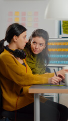 Obraz premium Confident women photo editors sitting at workplace in creative studio retouching photo, art director explaning color greding technic. Retouchers editing with drawing tablet and stylus pencil