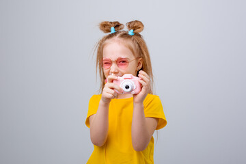little girl in sunglasses traveler holds a camera on a white background. Funny cute little girl in...