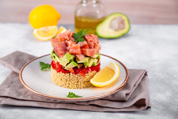Salmon tartare with tomatoes, avocado and quinoa on a plate and light gray table
