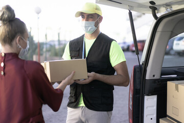 Portrait of delivery man wearing face protective mask for coronavirus spread prevention. Woman hand accepting a delivery of boxes from deliveryman.