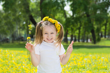 a little girl in a wreath with a dandelion in a spring park