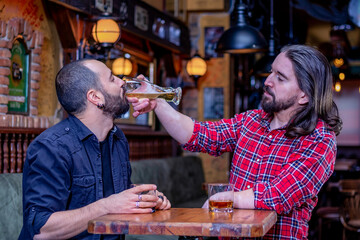 Two male friends drinking whiskey and beer together at the pub. Mates are drunk and they douse each other with beer.